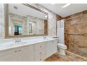 Bright bathroom featuring dual sinks, white cabinetry, tiled shower, and decorative wallpaper at 5856 Helicon Pl, Sarasota, FL 34238