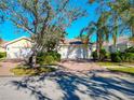 Single-story home with a two-car garage, brick driveway, lush landscaping, and mature trees at 5856 Helicon Pl, Sarasota, FL 34238