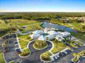 Aerial view of the clubhouse, golf course, and lake surrounded by lush landscaping and parking areas at 1298 Highland Greens Dr, Venice, FL 34285