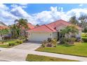 Beautiful single-story home featuring a red tile roof, a two-car garage, lush landscaping, and a well-manicured lawn at 446 Pinewood Lake Dr, Venice, FL 34285