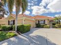 Inviting single-story home with a terracotta tile roof, manicured bushes, and an attached two-car garage at 174 Treviso Ct, North Venice, FL 34275