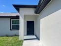 Close-up view of a modern front door with neutral stucco and dark trim and a well manicured lawn at 12316 Durango Ave, North Port, FL 34287