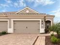 Close up of a three car garage with a brick paver driveway and manicured landscaping at 11575 Okaloosa Dr, Venice, FL 34293
