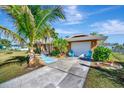 Inviting home exterior featuring a concrete driveway, blue Adirondack chairs, and lush tropical landscaping at 13534 Alberta Ave, Port Charlotte, FL 33981