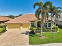 A picturesque exterior showcases a yellow home featuring palm trees, brick driveway, lush landscaping, and a clay tile roof at 1662 Bobcat Trl, North Port, FL 34288