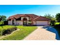 Beautiful single-story home with manicured lawn, tile roof, arched entryway, and brick driveway at 1886 Killdeer Ct, Venice, FL 34293
