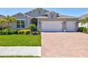 Well-maintained single Gathering home with a 3-car garage, brick driveway, landscaping, and blue door at 1606 Cedar Valley Dr, Port Charlotte, FL 33953