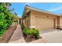 Beige home featuring a one-car garage, tile roof, and tropical landscaping with a brick walkway at 335 Auburn Woods Cir, Venice, FL 34292