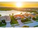Stunning aerial view of a waterfront home with lush landscaping during a vibrant sunset over the lake at 109 Montelluna Dr, North Venice, FL 34275