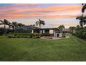 Picturesque backyard with a screened-in lanai, outdoor seating area, lush green lawn, and tropical landscaping at sunset at 19893 Cobblestone Cir, Venice, FL 34292