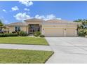 Beautifully landscaped yellow home with tile roof and a wide driveway leading to a two-car garage at 615 May Apple Way, Venice, FL 34293