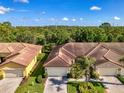 An aerial view of a villa with a tile roof, a paver driveway, a well-manicured lawn, and lush landscaping at 11096 Campazzo Dr, Venice, FL 34292