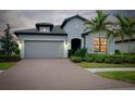 Elegant single-story home with a brick driveway, professional landscaping, and a warm glow from interior lights at 1565 Hyssop Loop, North Port, FL 34289
