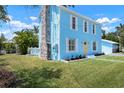 Light blue home features a stone chimney, a welcoming yellow door, and lush green lawn with flower beds at 121 Dolly St, Punta Gorda, FL 33950