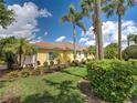 Charming yellow home with a red tile roof, lush landscaping, and elegant palm trees against a blue sky at 13150 Huerta St, Venice, FL 34293