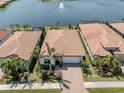 Aerial view of a single-story home with a brick driveway and a serene waterfront view of a lake with a fountain at 149 Vinadio Blvd, Nokomis, FL 34275