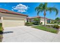 Home exterior view featuring a two-car garage, driveway, and manicured tropical landscaping at 11186 Batello Dr, Venice, FL 34292