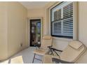 Cozy covered patio with two comfortable chairs, a window with shutters, and a view into the home at 11186 Batello Dr, Venice, FL 34292