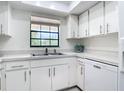 Bright kitchen features white cabinetry, stainless steel sink, neutral countertops, and views of the trees outside at 1730 Manasota Beach Rd # 212, Englewood, FL 34223