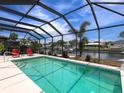 Screened-in pool area with a beautiful waterfront view and two red lounge chairs at 18302 Burkholder Cir, Port Charlotte, FL 33948