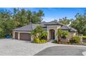 Beautiful home showcasing a paver driveway, three-car garage, and meticulously landscaped yard with palm trees and colorful flowers at 5850 Saddle Oak Trl, Sarasota, FL 34241
