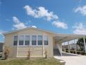 Charming, light yellow single-Gathering home with attached carport, lush green grass, and bright blue sky at 554 Aspen Ave, Venice, FL 34285