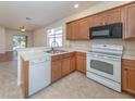 Kitchen featuring light wood cabinets, stainless sink, white appliances, and an open view to the living room at 11649 Tempest Harbor Loop, Venice, FL 34292