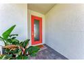 A bright orange front door welcomes you, complemented by lush greenery and a textured white wall at 12816 Morning Mist Pl, Venice, FL 34293