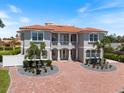 Elegant two-story home with a red tile roof, white columns, a balcony, and a paver driveway with lush landscaping at 2322 Bayshore Rd, Nokomis, FL 34275