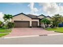 Charming single-story home boasts a three-car garage, tiled roof, brick driveway, and lush landscaping at 13634 Vancanza Dr, Venice, FL 34293