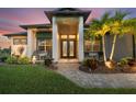Elegant home entrance with double doors, manicured landscaping, brick pathway, and inviting exterior lighting at sunset at 14398 Fort Worth Cir, Port Charlotte, FL 33981