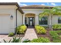 Charming home entrance with a brick walkway, lush landscaping, and decorative columns at 20443 Cristoforo Pl, Venice, FL 34293
