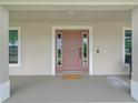Covered front porch with a stylish pink front door, sidelights, and neutral exterior at 7257 Maguire Ln, Englewood, FL 34224