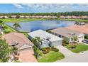 Aerial view of a bright, lakefront home showcasing a white tile roof and lush landscaping in a desirable community at 809 Derbyshire Dr, Venice, FL 34285