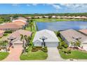 Lakefront home with a white tile roof, paver driveway, and mature landscaping, offering picturesque community views at 809 Derbyshire Dr, Venice, FL 34285