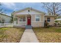Inviting home featuring a red door, covered porch, and well-maintained lawn with mature foliage at 3408 Phillips St, Tampa, FL 33619