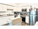 Well-lit kitchen boasts white cabinets, granite counters, stainless appliances, and a moveable island at 11856 Throttle Pl, Gibsonton, FL 33534