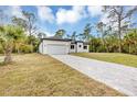 Charming white single-story home with a paved driveway surrounded by lush greenery on a sunny day at 18399 Hillsborough Blvd, Port Charlotte, FL 33954