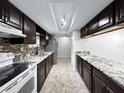 Galley kitchen featuring dark cabinets, granite counters, mosaic backsplash, and stainless-steel appliances at 8631 Cattail Dr, Temple Terrace, FL 33637