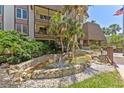 Condo exterior showcasing a landscaped water feature with palm trees and an American flag on a bright, sunny day at 3035 Countryside Blvd # 15B, Clearwater, FL 33761