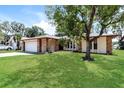 Single-story home boasts a well-manicured lawn with mature trees and stone accents on the facade at 12408 Golden Oak Cir, Hudson, FL 34669