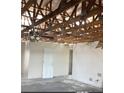 Interior view of a room with exposed ceiling beams, bare walls, a door, and damaged flooring at 3360 Peace River Dr, Punta Gorda, FL 33983