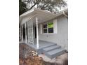 Side view of a gray painted brick home featuring a covered front porch with decorative ironwork and steps at 7240 Donna Dr, New Port Richey, FL 34652