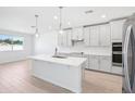 Contemporary kitchen with white cabinets, stainless steel appliances, a central island, pendant lights, and light wood flooring at 1799 Draughton Dr, Zephyrhills, FL 33541
