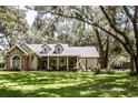 Inviting single-story home with stone detailing, dormer windows and a cozy front porch, framed by mature trees and lush green grass at 2906 Country Breeze Dr, Plant City, FL 33567