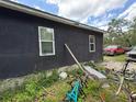 Side view of the house showing exterior wall, windows, and overgrown yard with bikes and miscellaneous items at 3613 Deleuil Ave, Tampa, FL 33610