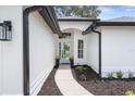 Inviting entryway with a modern white door, fresh landscaping, and sleek black gutters and light fixtures at 9555 Knightsbridge Cir, Sarasota, FL 34238