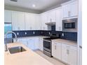 Well-equipped kitchen featuring modern appliances, white cabinets, light countertops and dark backsplash at 2729 Gabel Oak Dr, North Port, FL 34289
