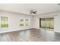 Living room featuring grey wood floors, neutral walls, ceiling fan, three windows, and sliding glass door at 12829 Scarlet Star Dr, Riverview, FL 33579