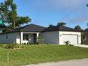 A new home shows off its verdant landscaping and white exterior with a dark roof at 4097 Feather Ter, North Port, FL 34286